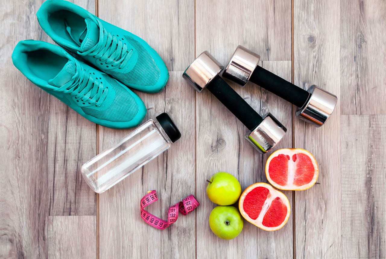 Shoes, weights, water bottle, and fruit laying on wood floor